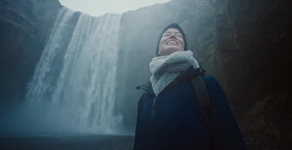 Woman smiles as she admires a large waterfall surrounded by mist and rocky walls