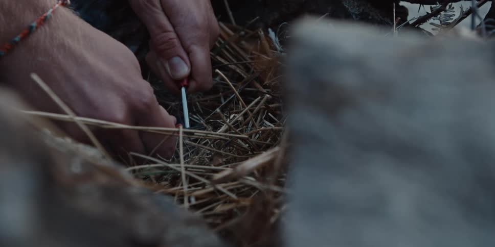 Person lights a fire by rubbing flint on dry straw between stones