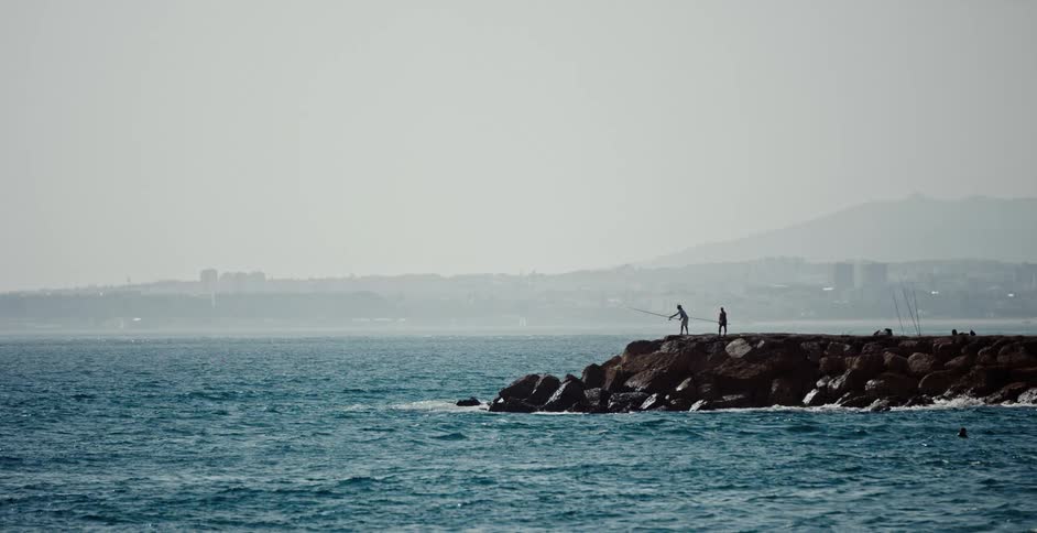 A couple people fishing off the end of a jetty
