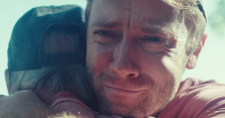Father and son hugging and crying in the front yard of a house on a sunny day