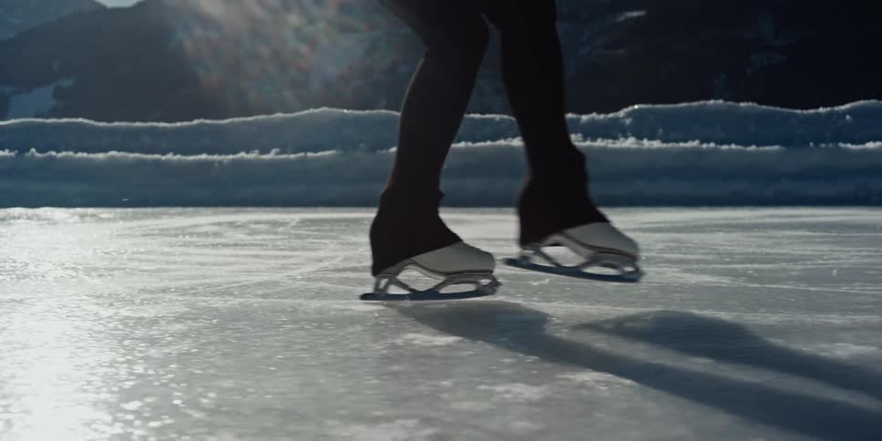 Ice skater skates across an outdoor ice rink located near the mountains on a winter day