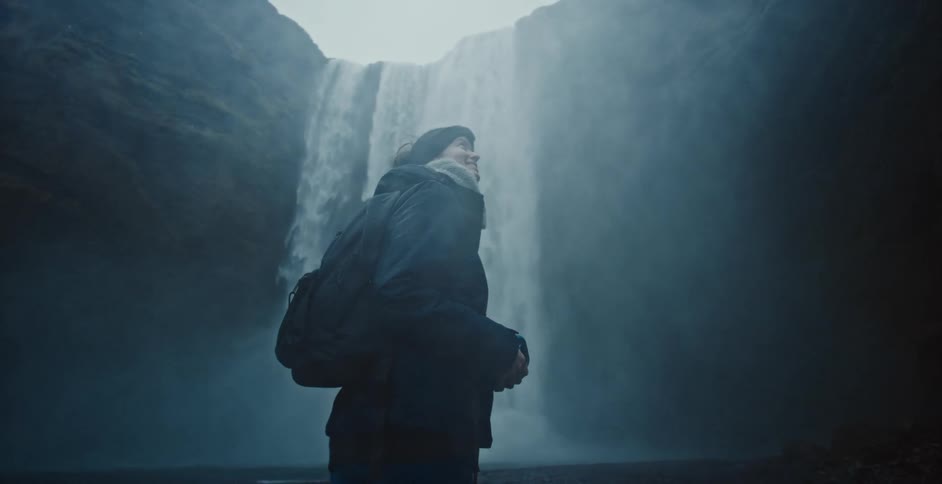 A woman stands at the bottom of a waterfall
