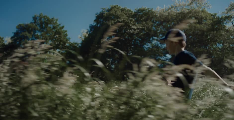 A kid wearing a hat and a blue tshirt runs quickly across a grassland at midday