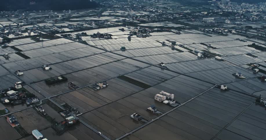 Flooded rice fields reflect the sky in a vast rural area divided by roads and small buildings