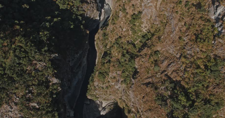 An aerial view of a stream flowing between mountainous rocks covered in grass and vegetation on a sunny day