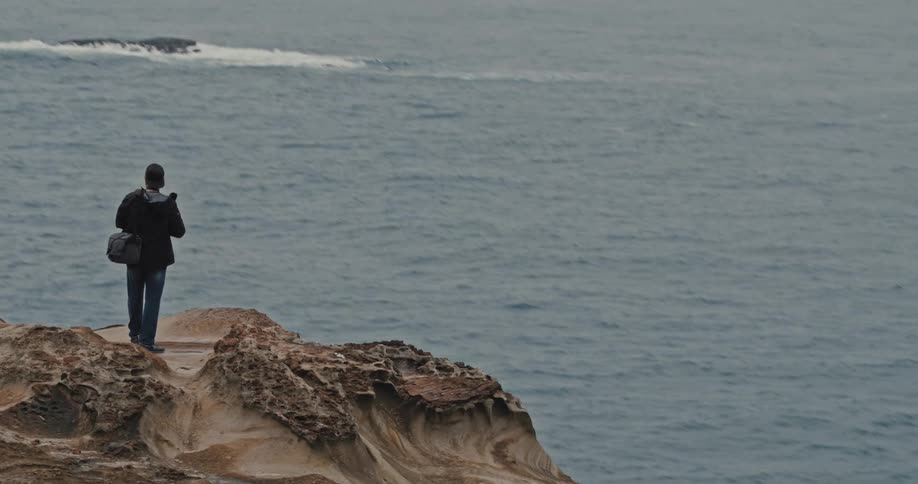 A footage of a man standing on a cliff by the sea side
