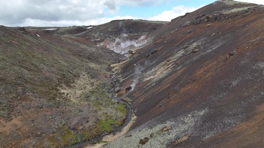 Fumaroles emerge from the ground in a geothermal valley surrounded by rocky hills and sparse vegetation