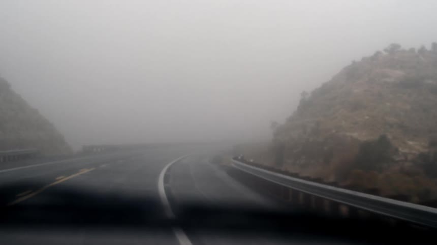 A car is traveling down a twisting foggy road