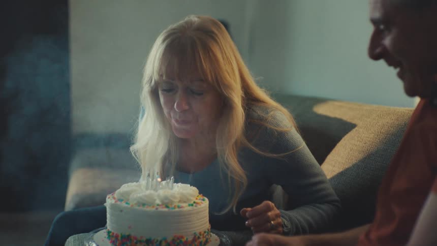 A woman blows out candles on a cake then smiles with the man