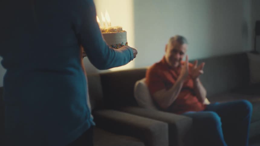 A woman brings a cake with candles to an older man