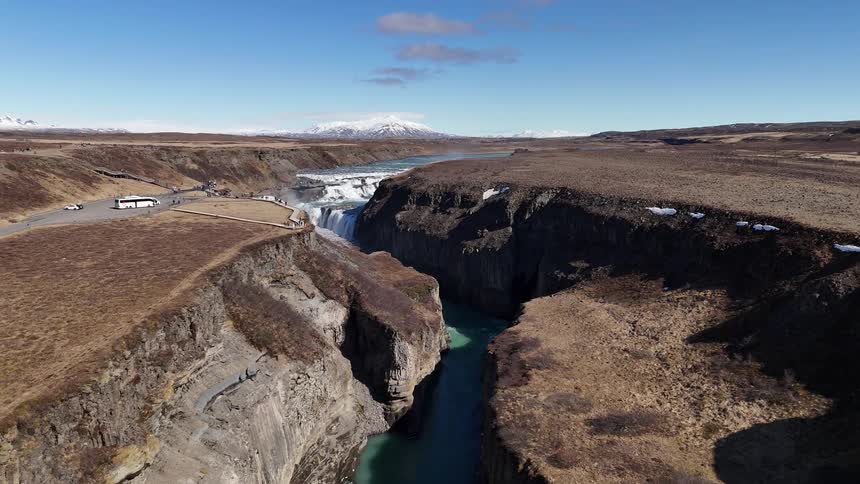 Bus parked at an overlook featuring a canyon with a waterfall feeding into its river