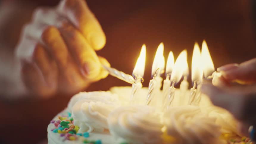Two people lighting candles on a birthday cake