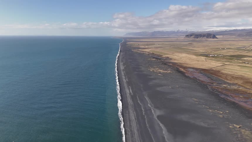 Aerial of ocean waves rolling into a beach with black sand