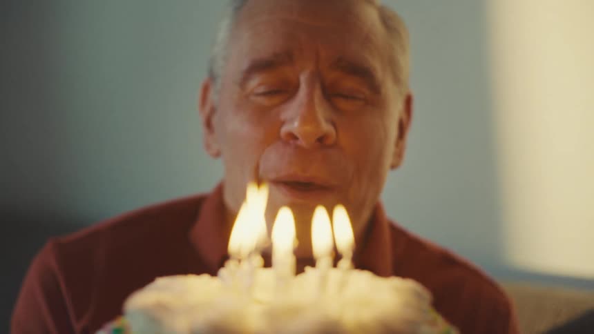 Husband happily blowing out candles on his birthday cake then kissing his wife