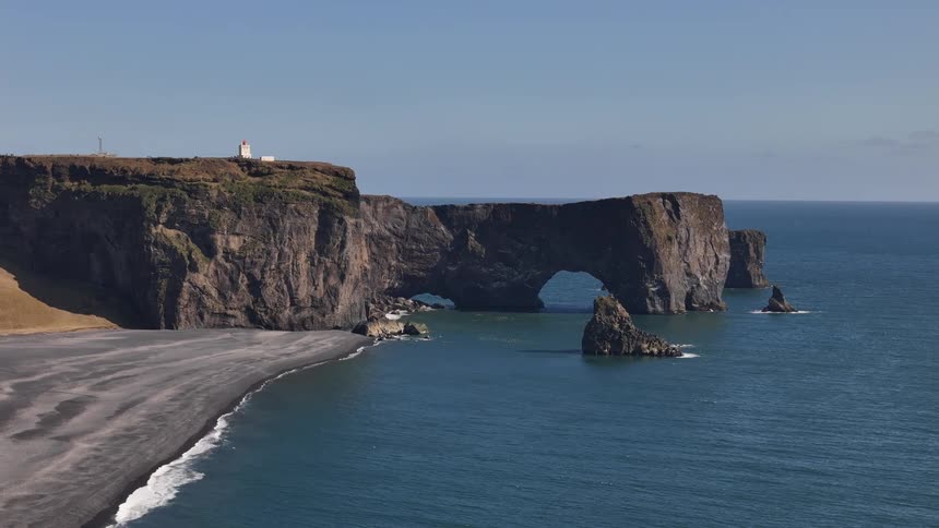 Buildings stand on a promontory extending into the ocean near a black sandy beach