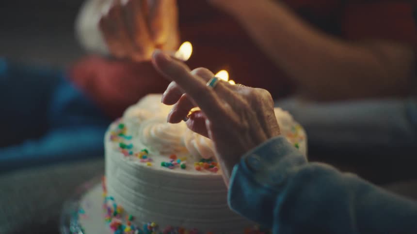Couple lighting candles on a small birthday cake at home