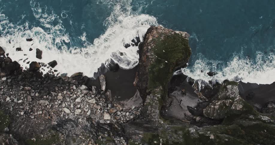 Birds eye view of waves crashing along steep rocky coastline