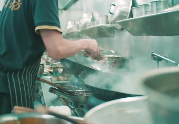 Chef prepares meals in large pots with intense steam in a busy industrial kitchen