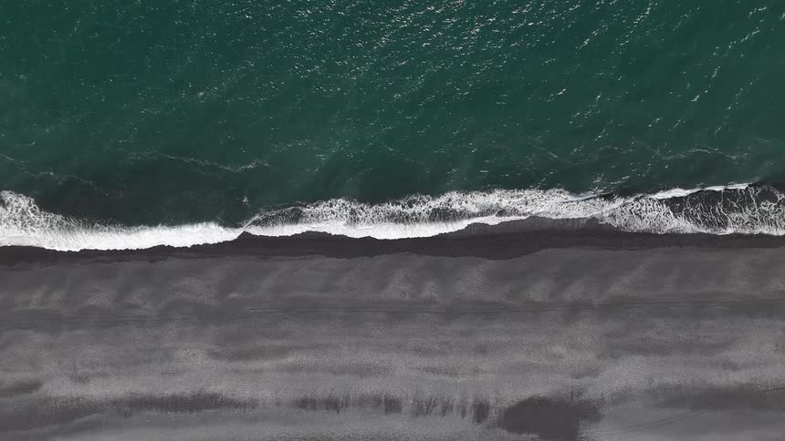 Birds eye view of waves rolling onto sandy shoreline at the beach
