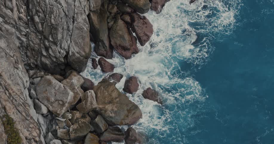 Waves crash along rocks at the bottom of a cliff