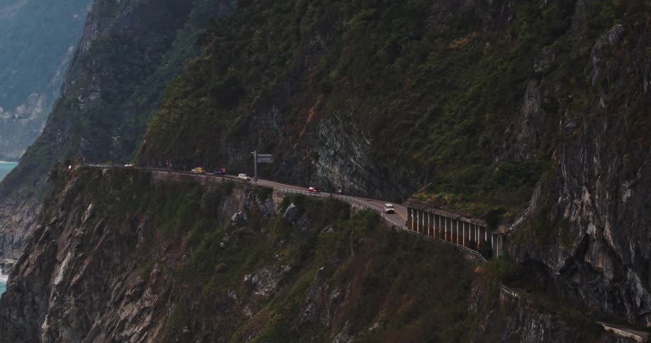 Aerial of cars driving along a coastal highway into a tunnel