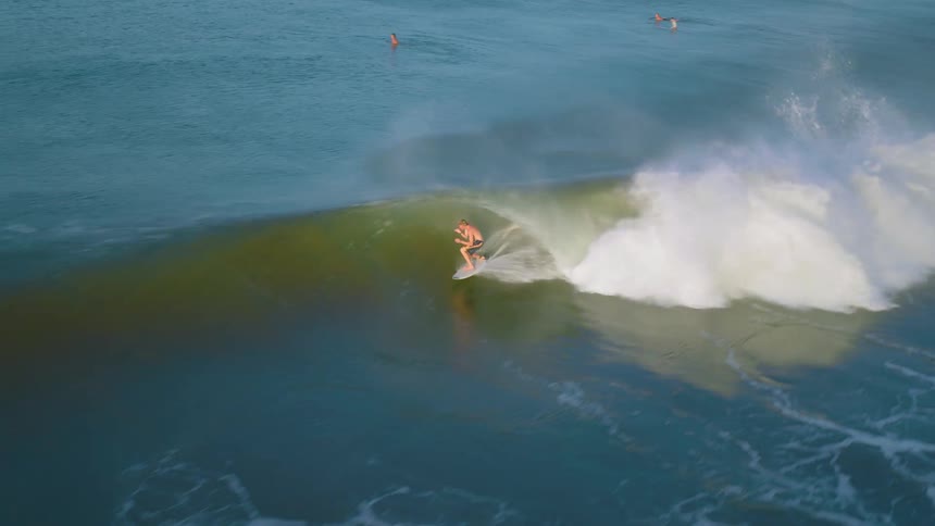 A man catches a barrelling wave on a surfboard and rides it out