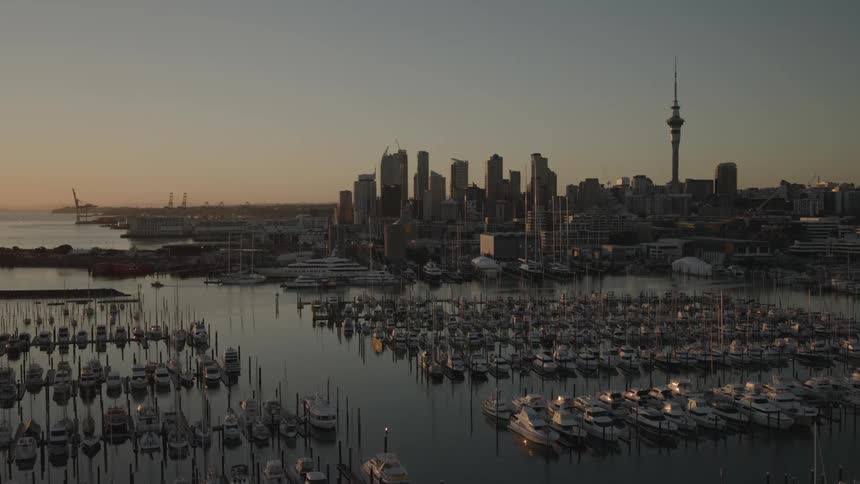 Boats fill a large marina located near a city skyline standing against a red horizon