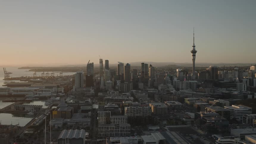A wide aerial shot captures aucklands skyline at sunset highlighting the sky tower