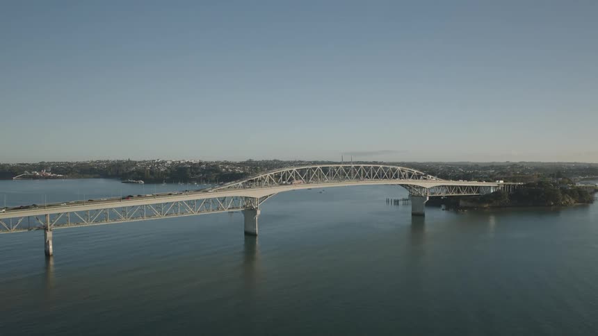 Aerial view of a long bridge spanning calm water under a clear blue sky