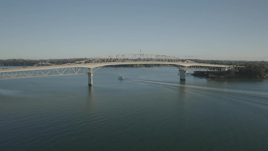 Yacht crosses under a busy bridge during the daytime