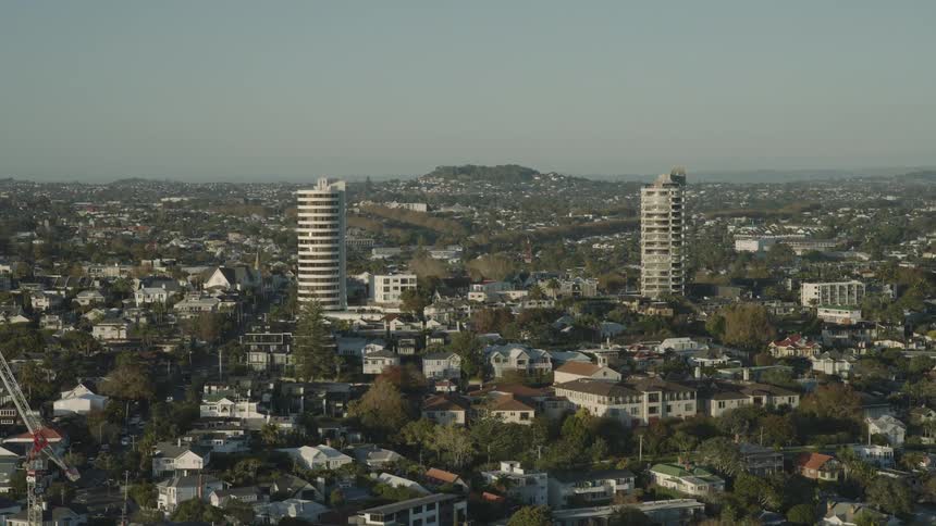 Traffic passes through a residential area containing houses and apartment buildings during the daytime