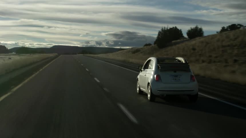 A car driving down a road with nothing but open fields on the sides