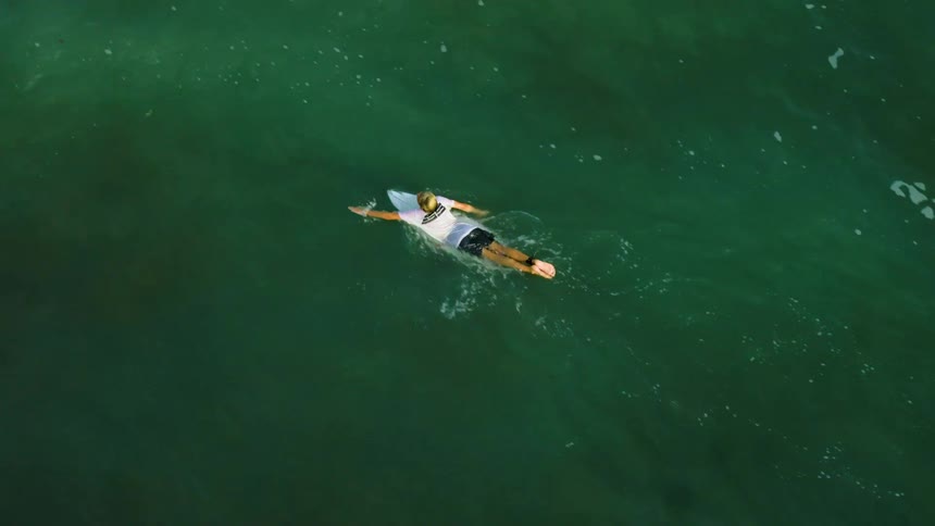 A person is laying on a surfboard paddling in the ocean