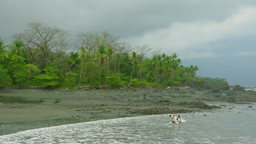 Three teenage boys are walking into the water at a beach with surfboards