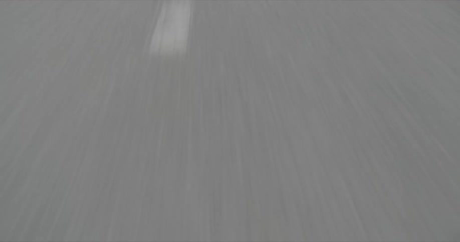 From a drivers perspective the view focuses on the grey asphalt whizzing by below with white street markings blurring due to the rapid speed