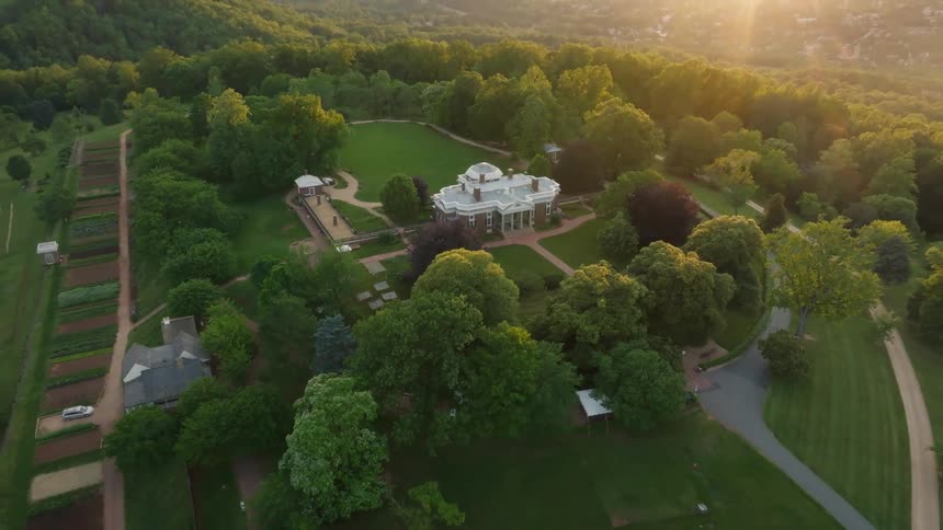 Monticello a palladianstyle mansion with white columns and a dome sits atop a verdant hill surrounded by trees and cultivated land under a soft clear sky