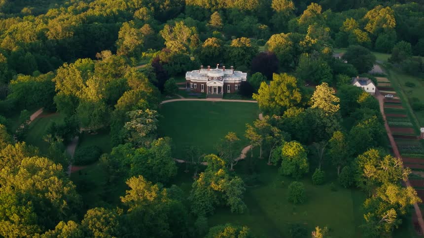 Aerial shot of a historic mansion surrounded by lush green forest and farmland