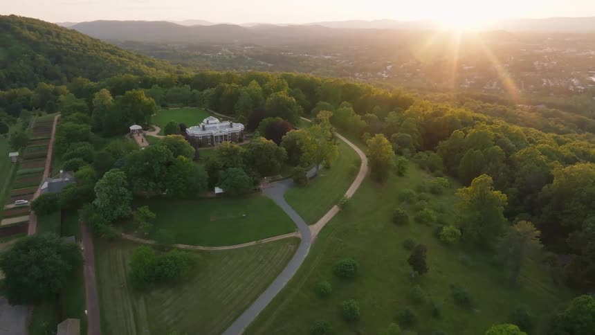 Aerial view of a historic countryside estate surrounded by trees farmland and sunrise lighting