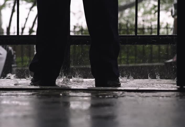 Two pairs of legs in dark pants and shoes walk on a wet surface in the rain