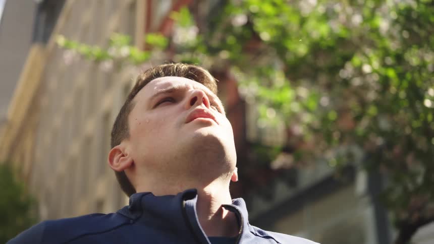 A man standing on a street near residential buildings stretching his neck