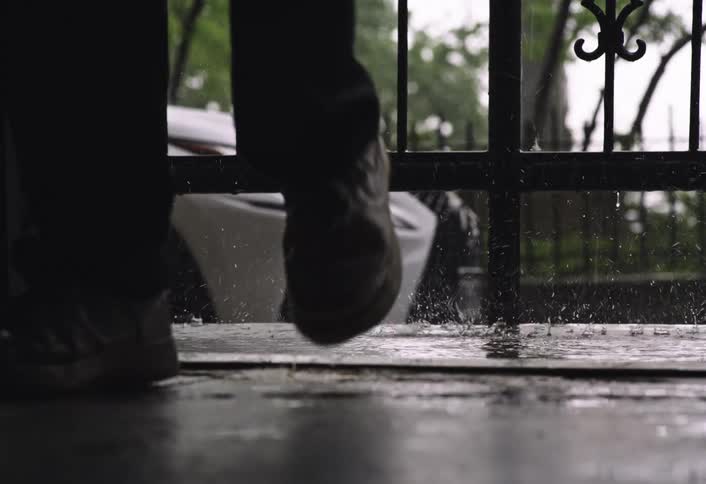 A person walking in the rain near a fence