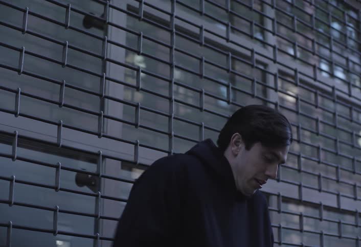 A man in a black coat is standing outside and he is cold then he takes out his cell phone to look at it