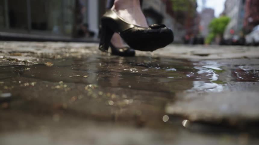 Woman wearing high healed shoes walks through a puddle on a city street during the daytime