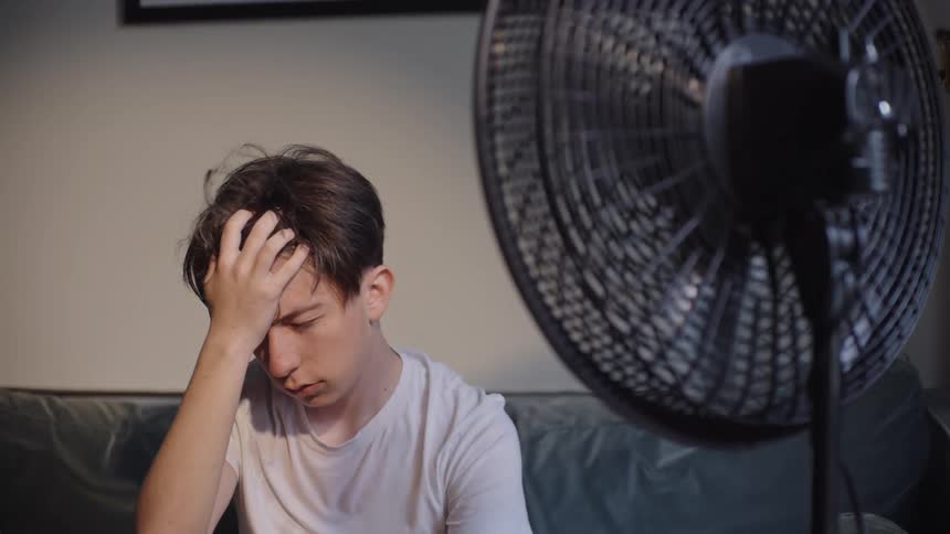 A teenager is hot and sitting in front of a fan