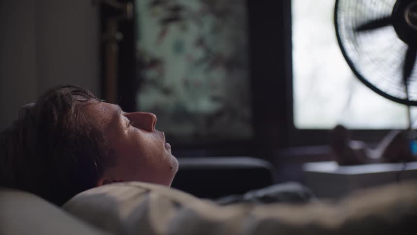 A man is sleeping on the couch in front of a fan