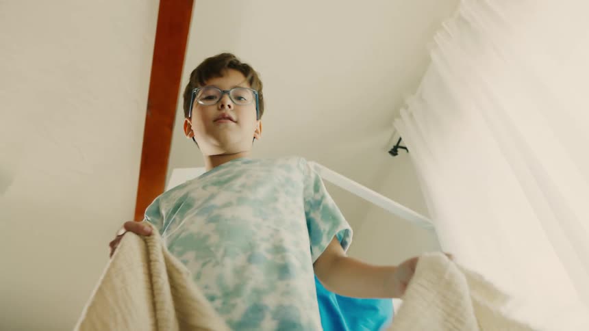 A boy shushes someone and drops a blanket on them