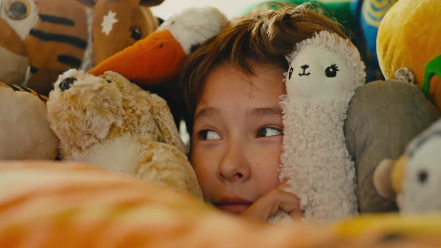 A boy is hiding in pile of stuffed animals