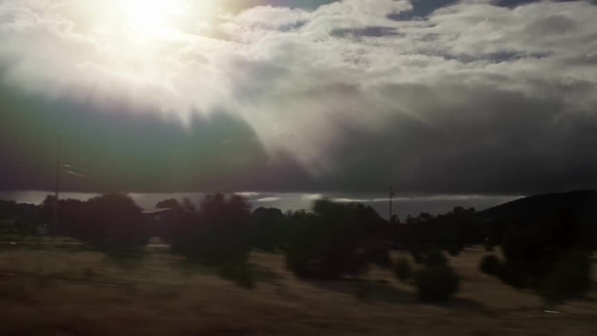 A view of the coast with the sun high in the sky as someone is driving by