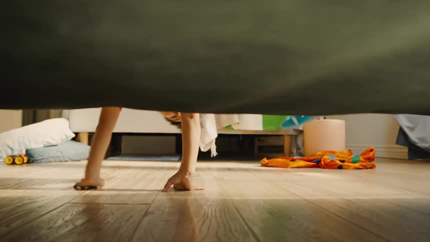A boy hands off the bed to look underneath