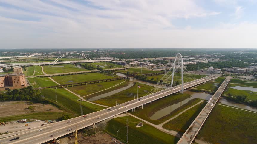 A series of cars driving across a bridge leading into the city at midday